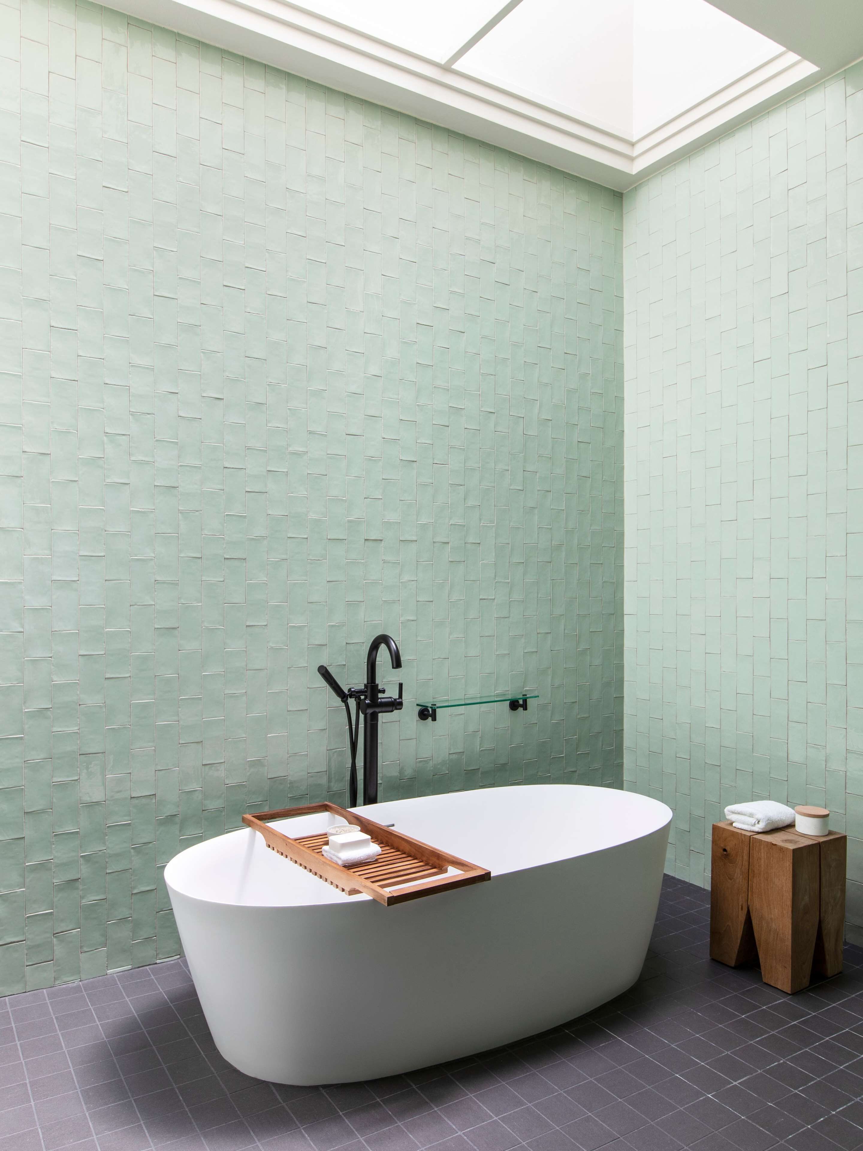 A modern bathroom with a freestanding bathtub, a glass shelf, and a wooden stool.