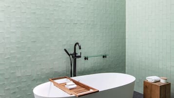 A modern bathroom with a freestanding bathtub, a glass shelf, and a wooden stool.