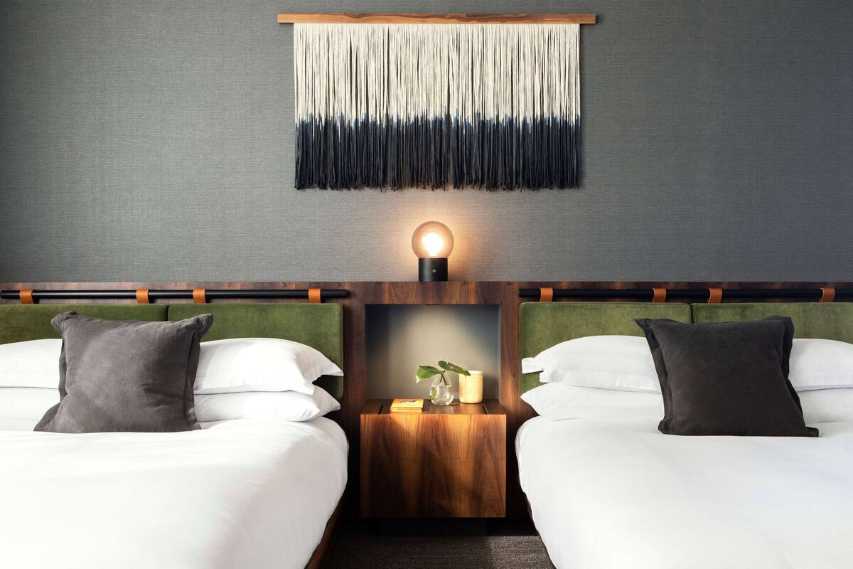 Une chambre d’hôtel avec deux lits, une lampe fixée au mur, une petite table de chevet en bois et un élément décoratif mural.
