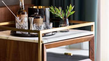 A bar cart with a bottle of Hudson Manhattan, a glass, and a small vase with green leaves.