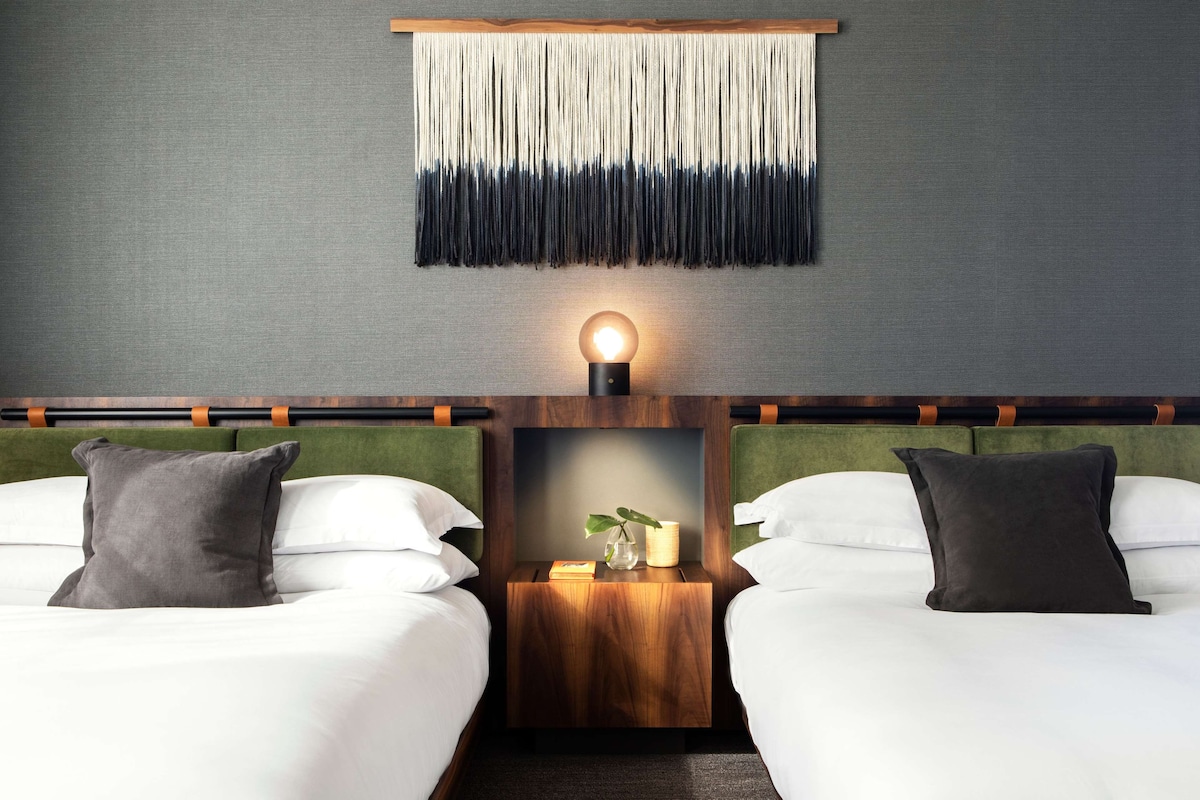 Une chambre d’hôtel avec deux lits, une lampe fixée au mur, une petite table de chevet en bois et un élément décoratif mural.
