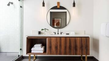 Un baño moderno con tocador de madera, espejo redondo y cabina de ducha de vidrio.