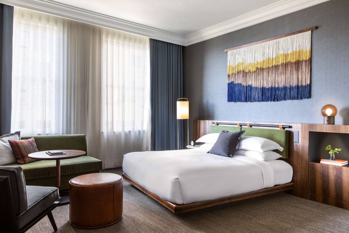 Une chambre d’hôtel avec un grand lit, un canapé vert, une petite table ronde et une lampe fixée au mur.