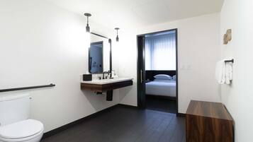 A modern bathroom with a toilet, sink, and mirror. There is a wooden bench and a towel rack on the wall.
