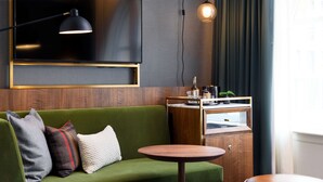 Un canapé vert avec trois coussins, une petite table d’appoint en bois, un téléviseur fixé au mur et un meuble avec un miroir.