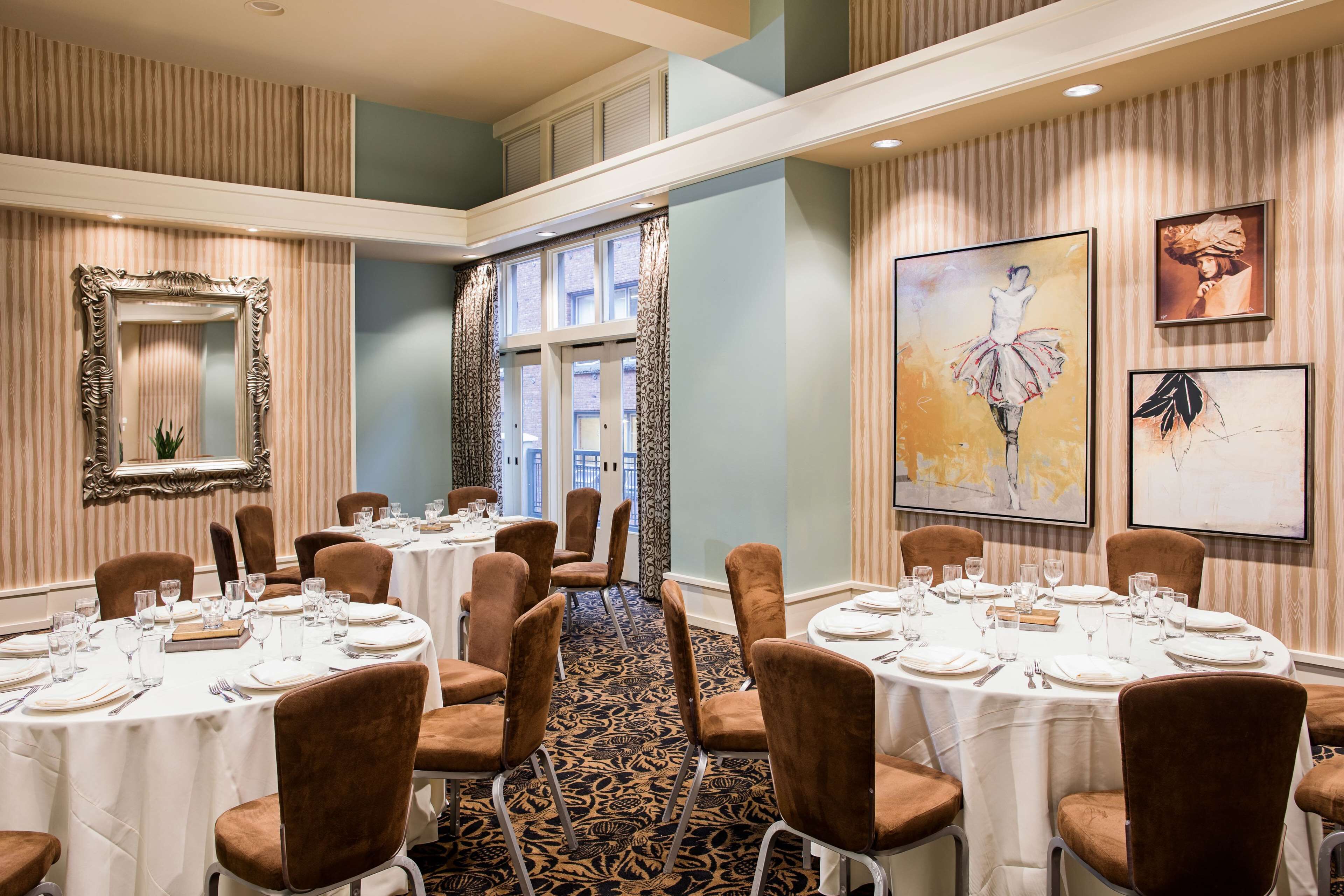 Un espace repas avec des tables rondes disposées pour accueillir six personnes, des chaises à l’assise rembourrée de couleur marron et un tapis à motifs.