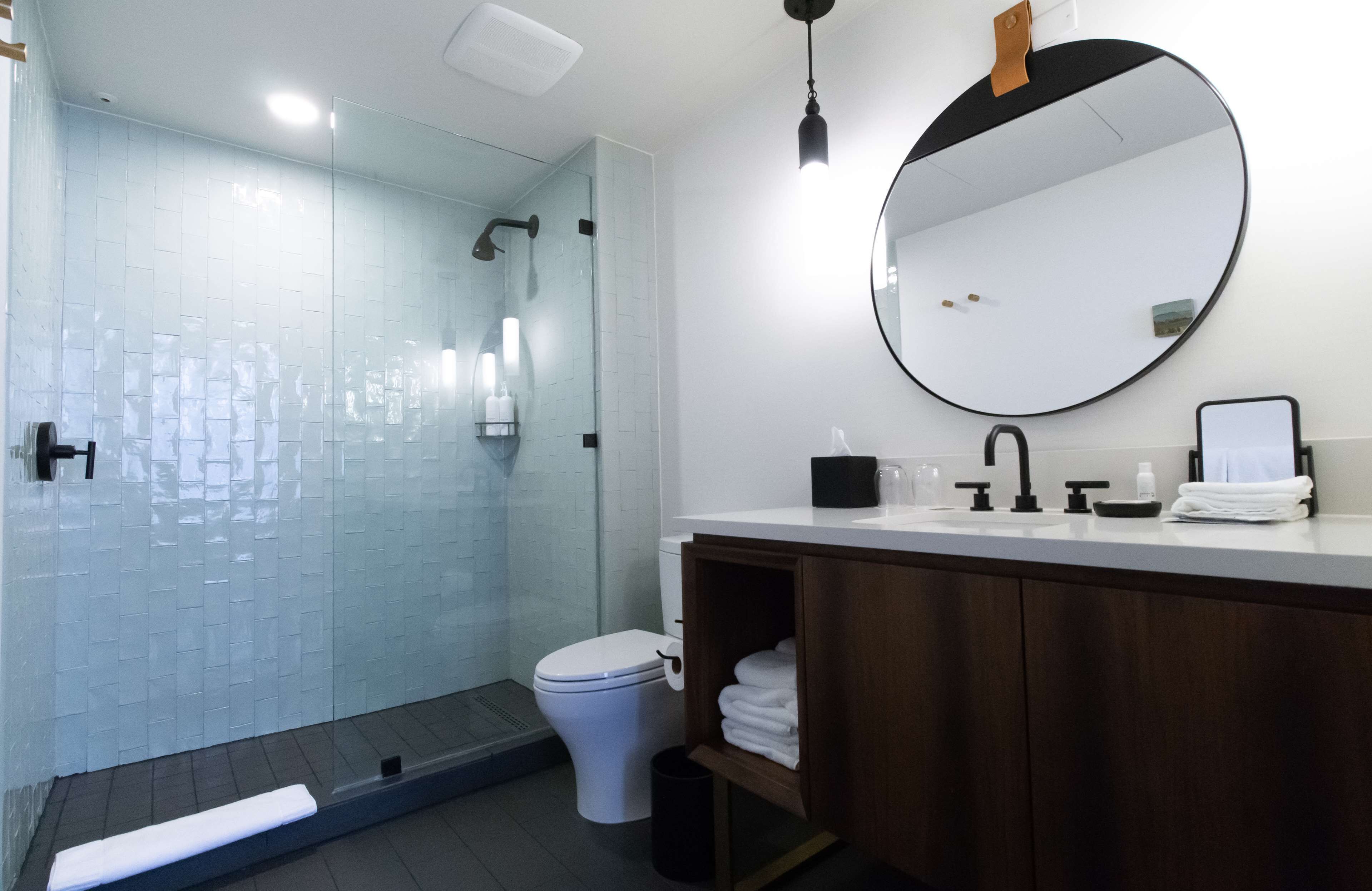 Un baño moderno con cabina de ducha de vidrio, inodoro blanco, tocador de madera y un perchero para toallas.