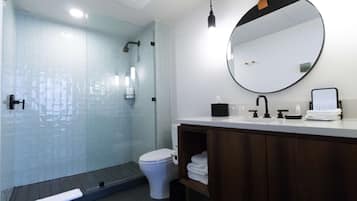 Un baño moderno con cabina de ducha de vidrio, inodoro blanco, tocador de madera y un perchero para toallas.