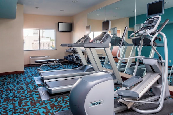 Un gimnasio con cintas de correr, un espejo grande y una ventana que da a edificios.