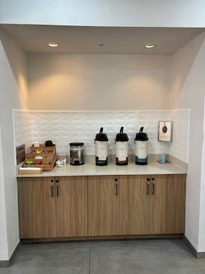 Cozinha com painel de azulejos brancos, armários de madeira e três máquinas de café marcadas com a inscrição 'Breathe'.