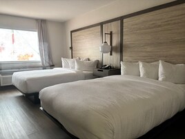 A hotel room with two beds, a nightstand, a lamp, and a window with curtains.