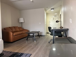 A modern living room with a brown leather sofa, a small table, and a desk with a chair.