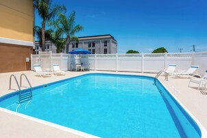 A rectangular swimming pool with a blue tile interior, surrounded by white lounge chairs and a white fence.