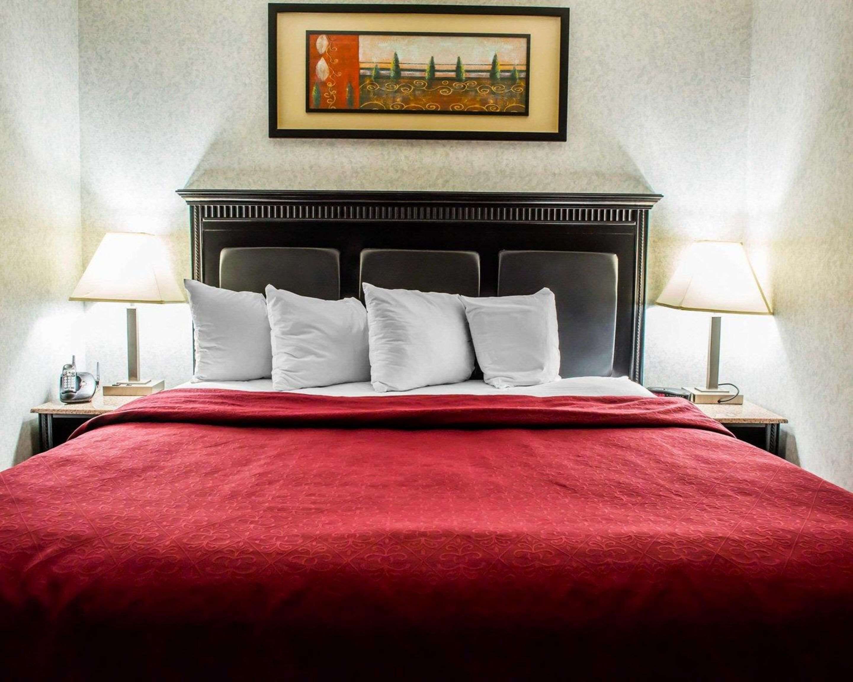 Habitación de hotel con una cama grande, un cabecero, dos lámparas de noche y un cuadro enmarcado en la pared.