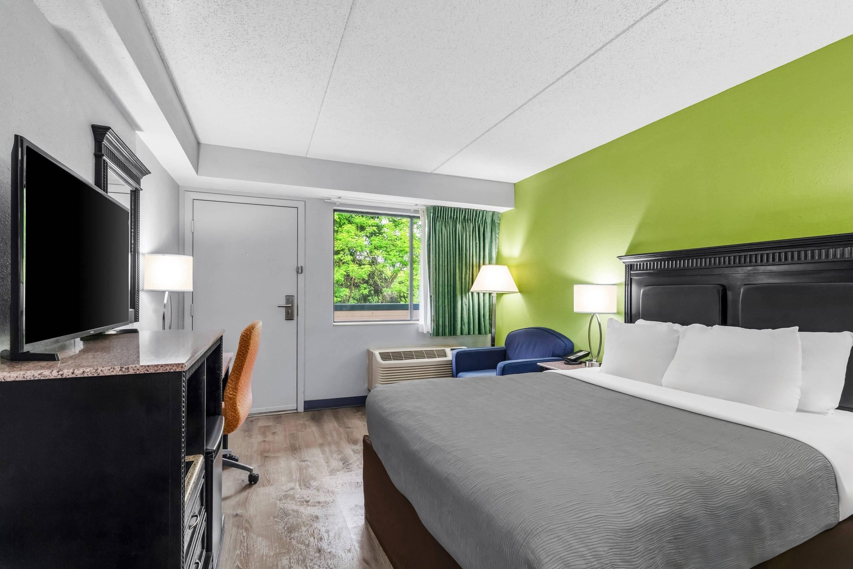 A hotel room with a bed, television, desk, chair, and a window with curtains.