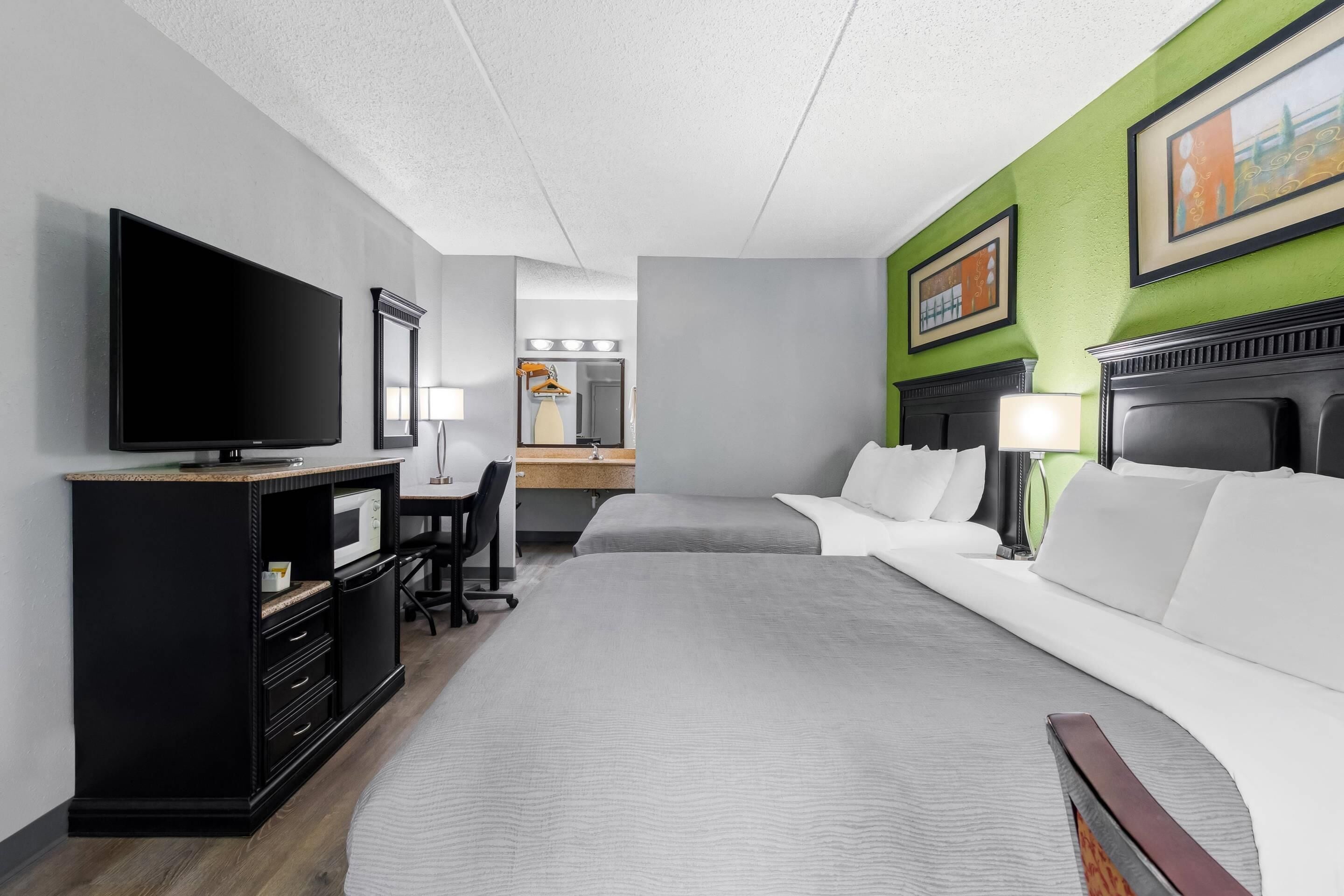 Quarto de hotel com uma cama, uma escrivaninha com computador, televisão e espelho.