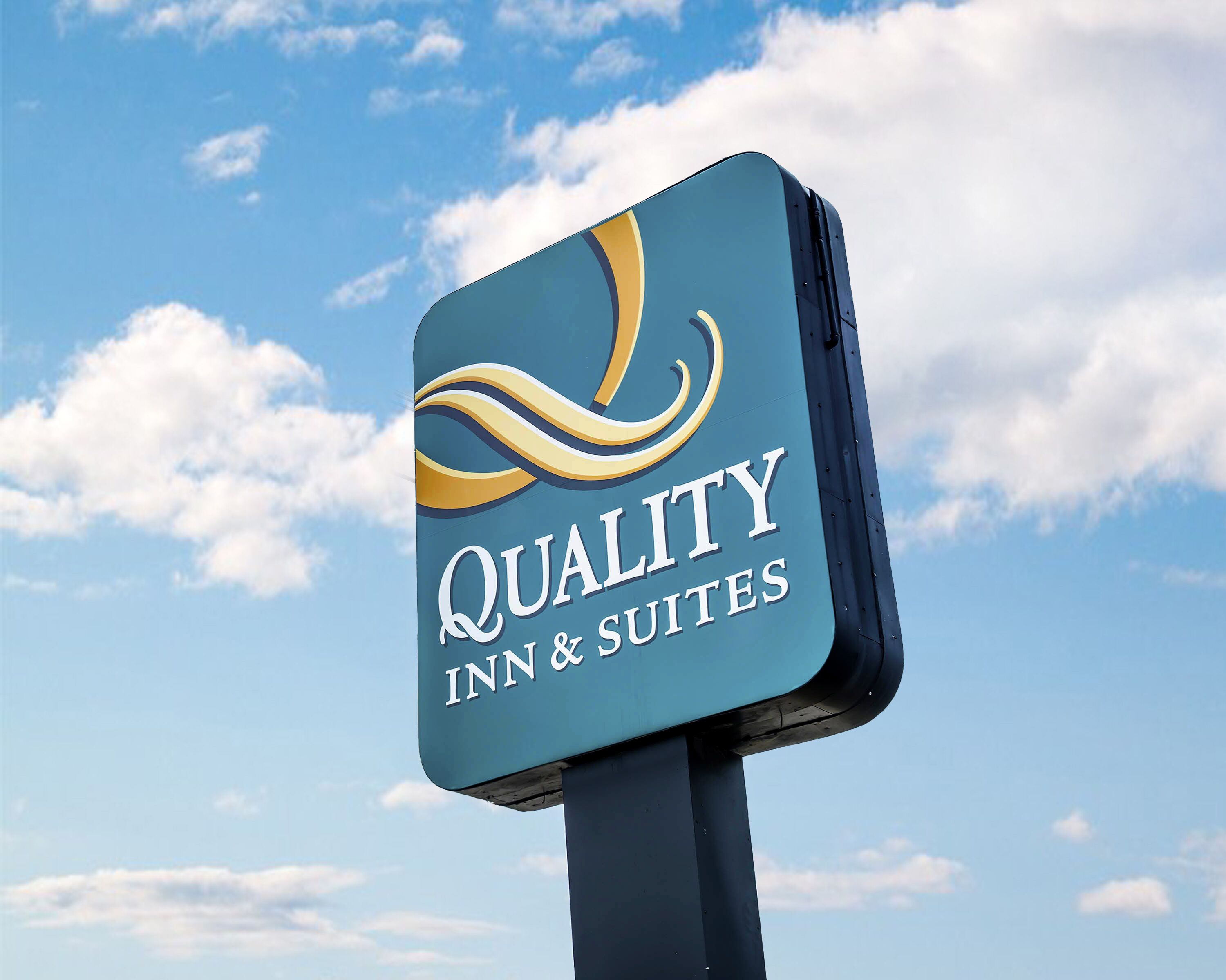 A sign for Quality Inn & Suites against a clear sky.