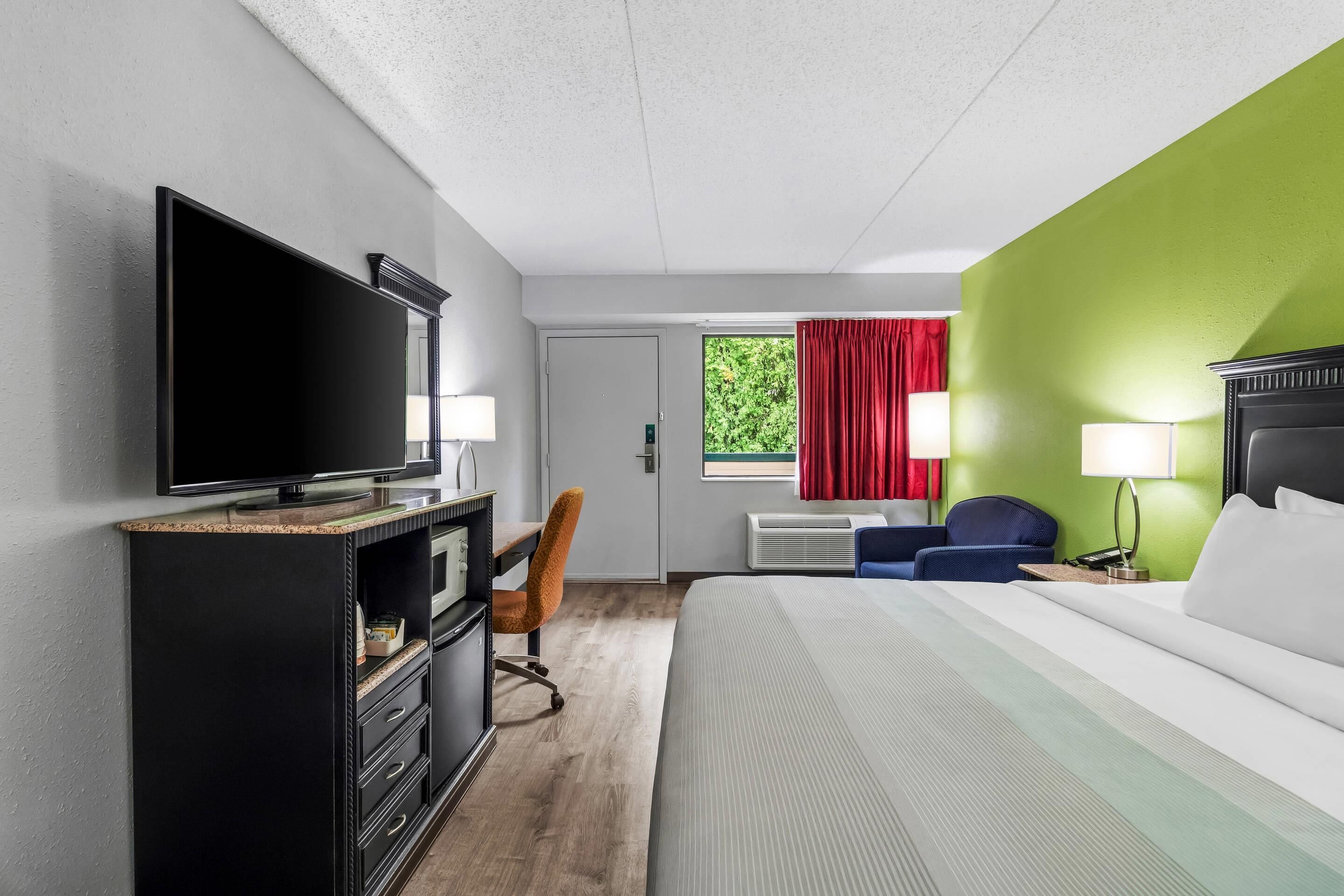 A hotel room with a bed, television, desk, chair, and a window with curtains.