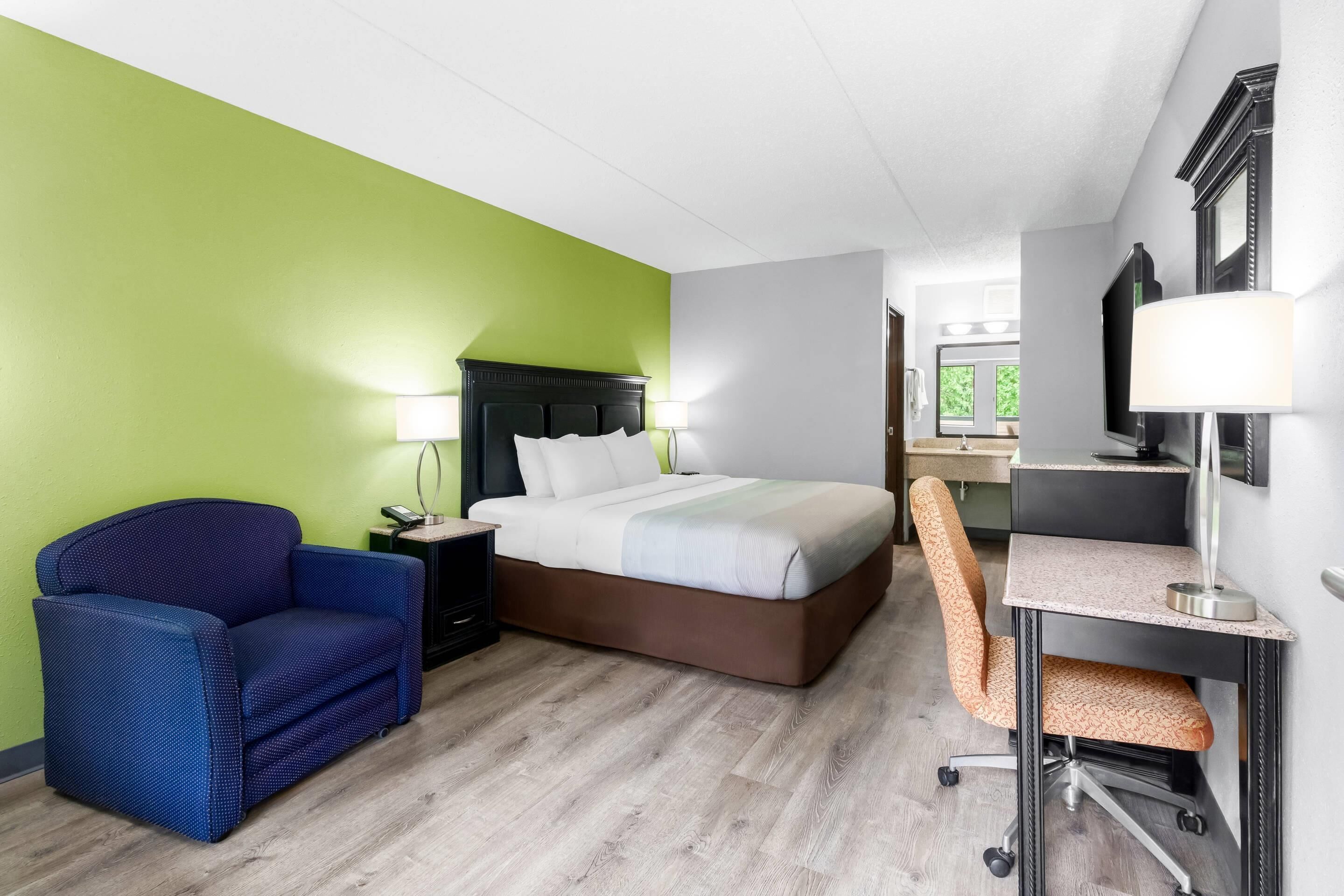Una habitación de hotel con cama, escritorio, silla, mesita de noche y lámpara.