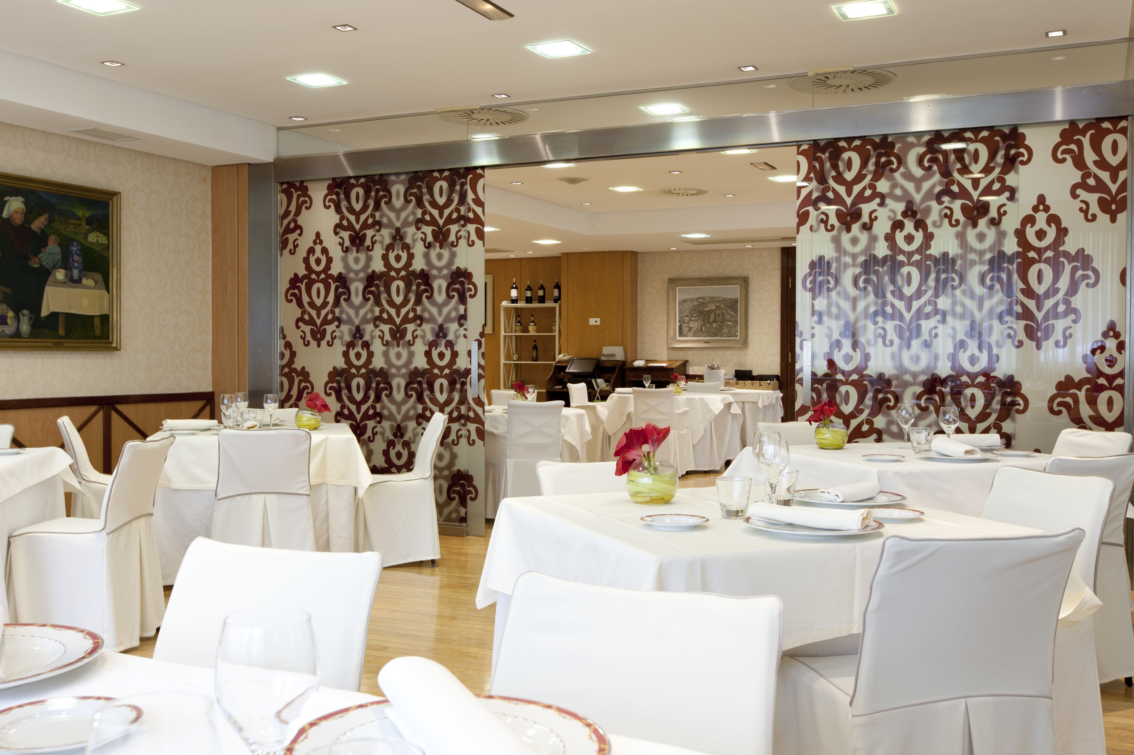 A banquet hall with round tables set for dining, white chairs, and a decorative wall with a patterned curtain.