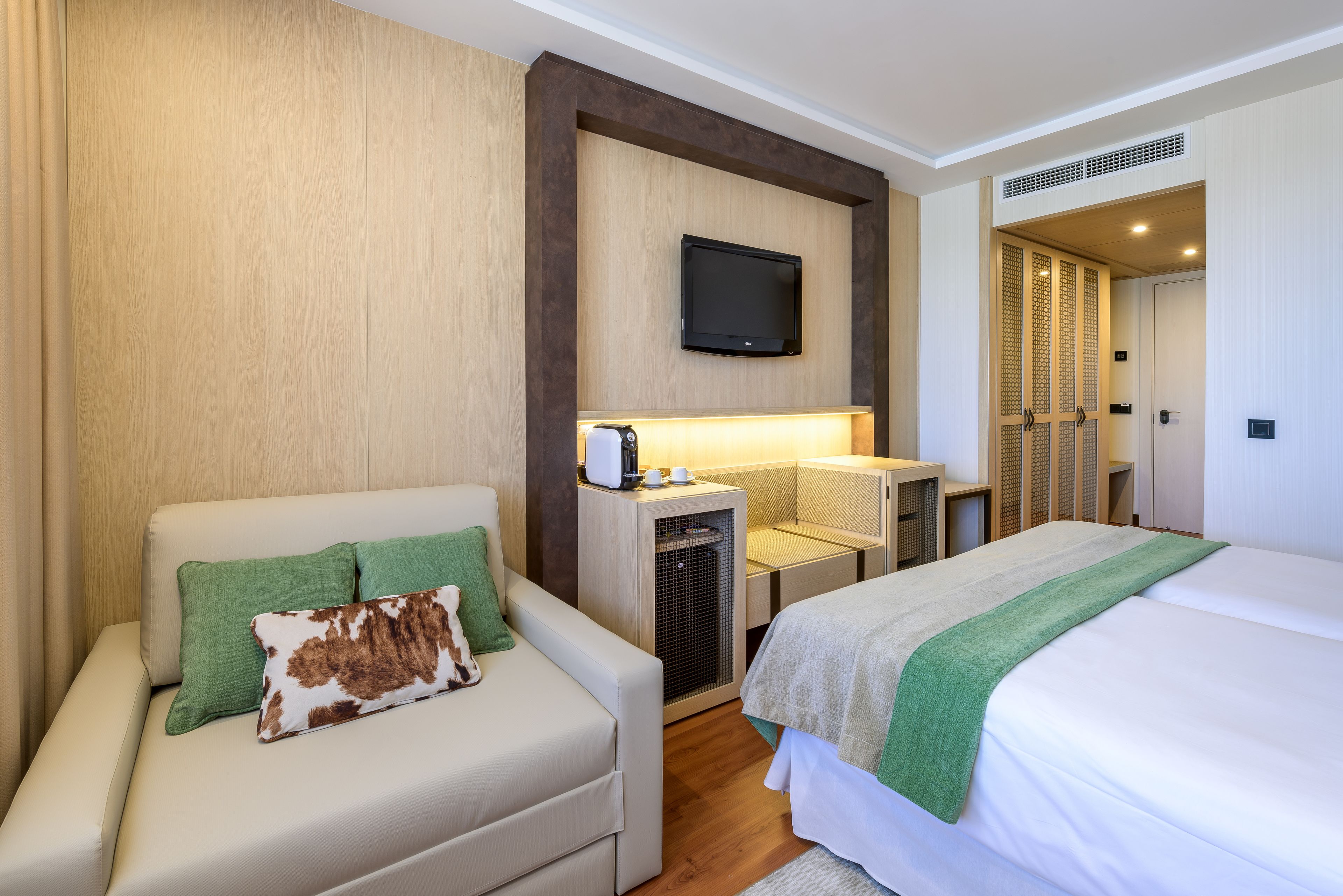 Une chambre d’hôtel comprenant un canapé, un lit, un téléviseur fix é au mur, une petite table avec une lampe et une armoire avec une porte coulissante.