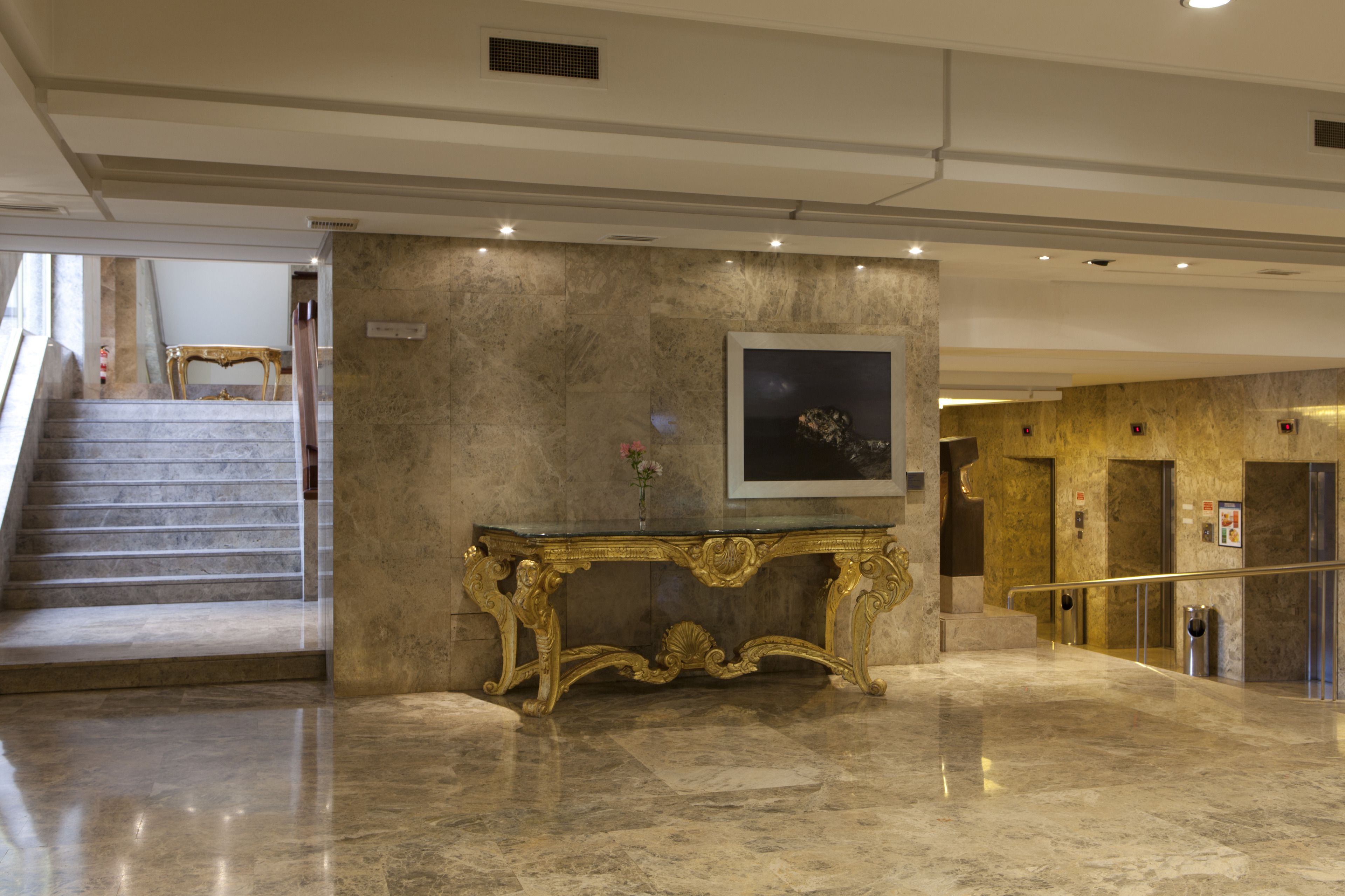 A marble-floored lobby with a grand staircase, a gold-accented console table, and a framed artwork on the wall.