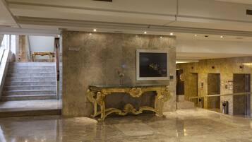 A marble-floored lobby with a grand staircase, a gold-accented console table, and a framed artwork on the wall.