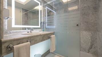 Un baño moderno con cabina de ducha de vidrio, encimeras de mármol y un espejo grande con iluminación integrada.