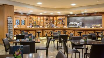 Un vestíbulo de hotel con una zona de bar, varias opciones de asientos y una exhibición de periódicos.