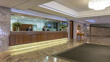 A reception area with a wooden counter, a large chandelier, and a television screen.