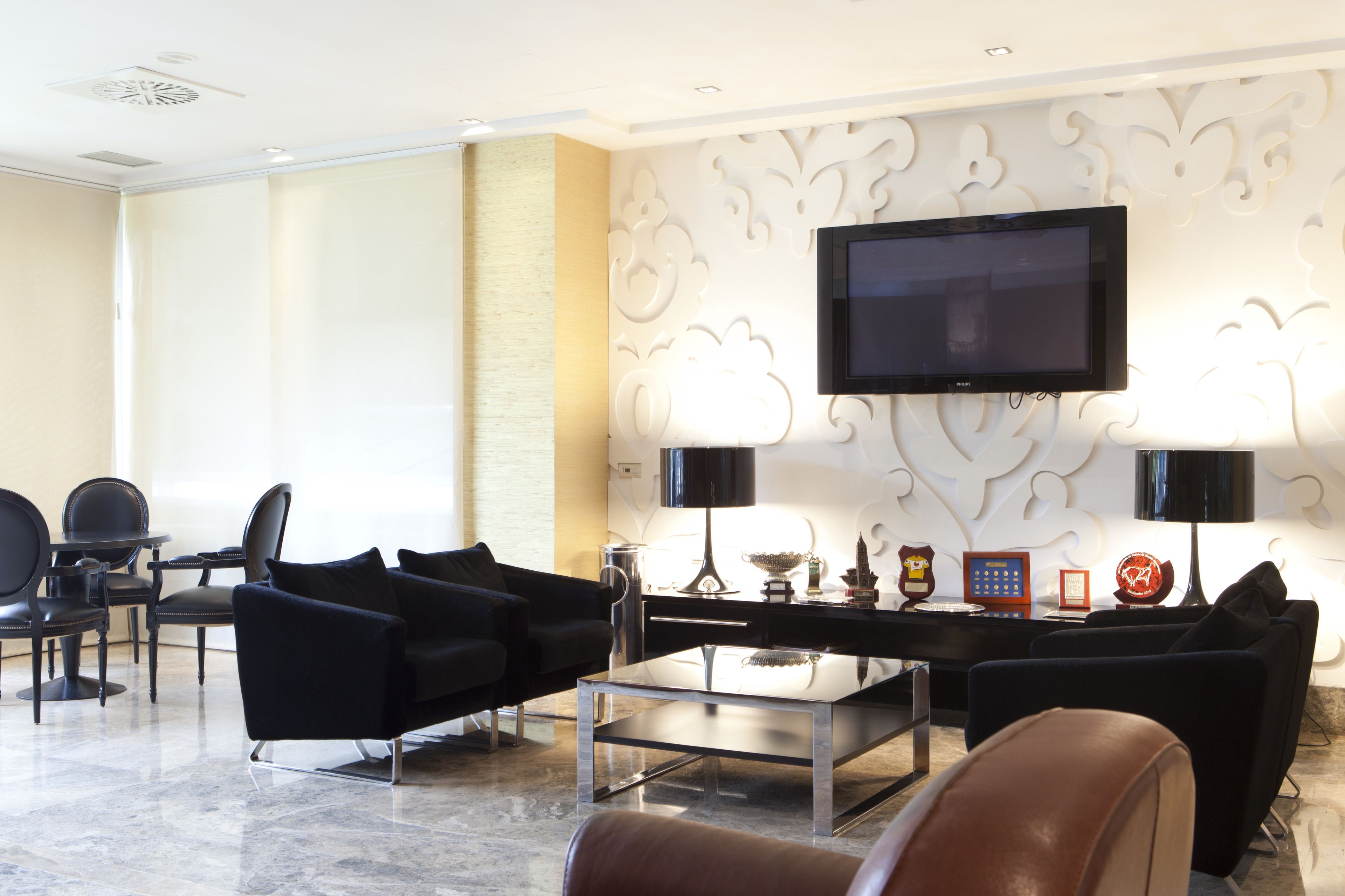 Un hall d’hôtel moderne, doté d’un téléviseur à écran plat fixé au mur, d’une table basse en verre et de canapés en cuir noir.