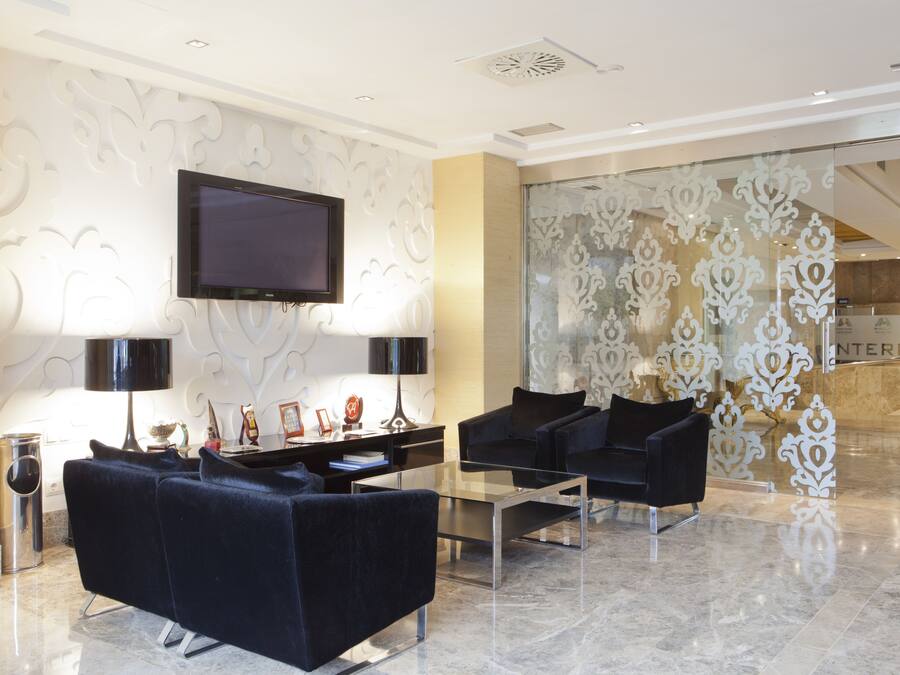 Eine moderne Lobby mit einem an der Wand befestigten Flachbildfernseher, einem Glastisch und zwei schwarzen Sofas, sowie einem dekorativen Glaseinsatz.