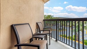A balcony with four chairs and a table, overlooking a parking lot and a bridge. - Best Western Oak Manor (Biloxi)