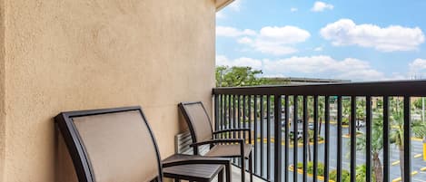 A balcony with four chairs and a table, overlooking a parking lot and a bridge.