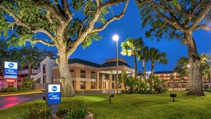 A Best Western hotel with a large tree in the foreground, a well-lit entrance, and a parking area visible in the background. - Best Western Oak Manor (Biloxi)