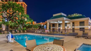 A swimming pool with lounge chairs and a mosaic table, surrounded by a fence and a building with a green roof. - Best Western Oak Manor (Biloxi)