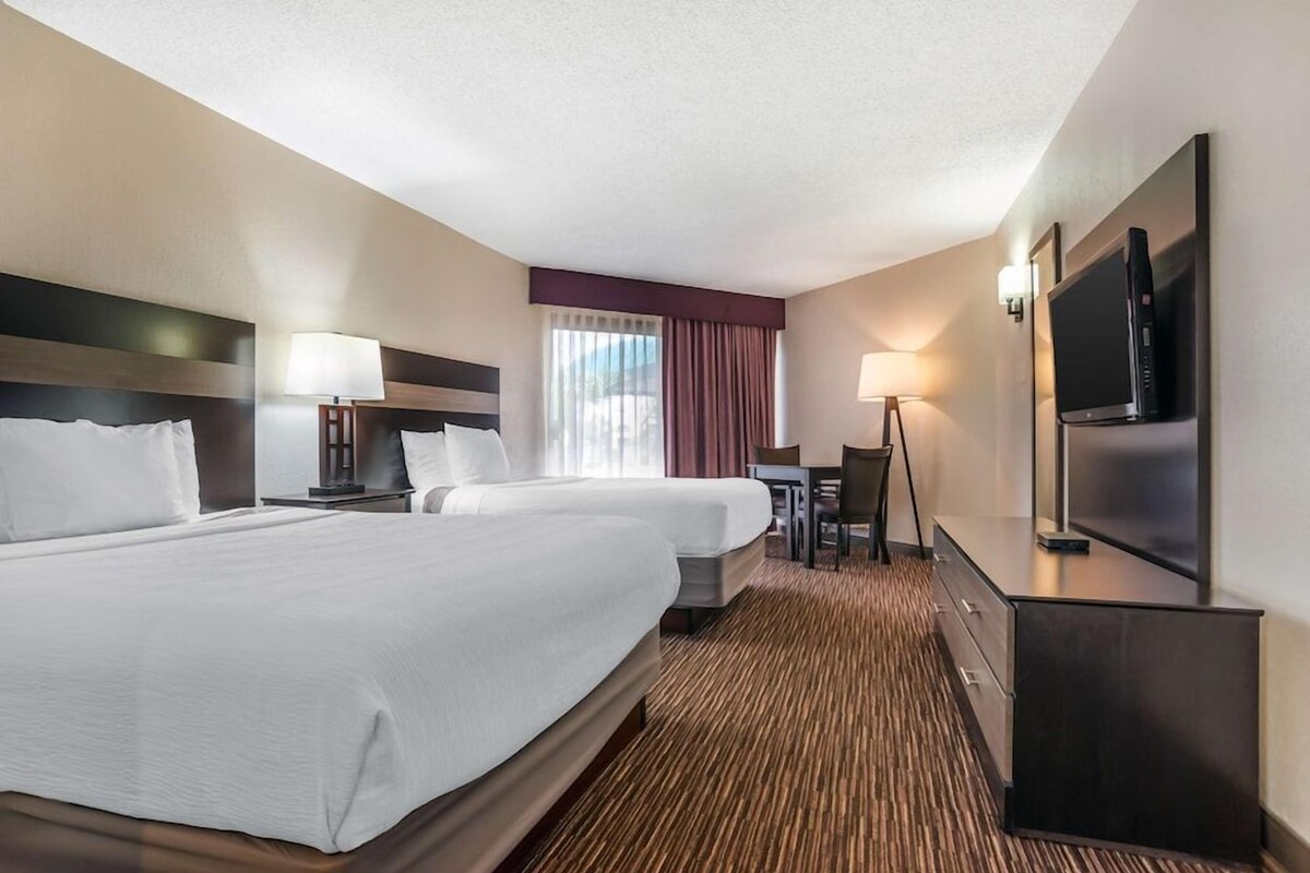 A hotel room with two beds, a desk, a chair, a TV, and a window with curtains.