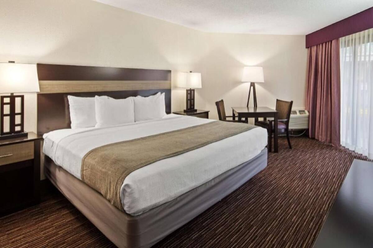 A hotel room with a large bed, bedside tables, a desk, chairs, and a window with curtains.