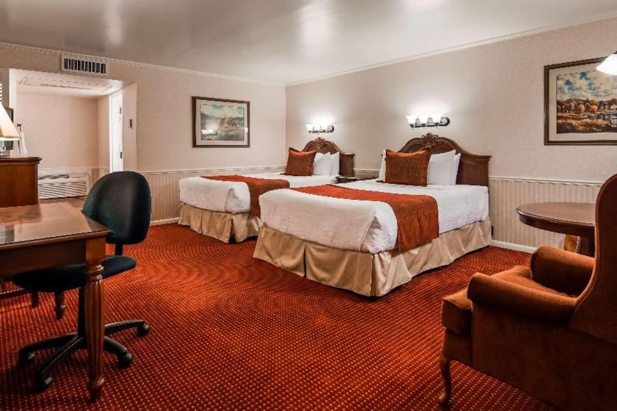 A hotel room with two beds, a desk, a chair, and a dining table.