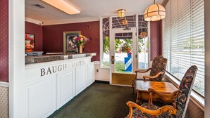 A reception area with a counter labeled "BAUGH MOTEL," a wooden chair, a table, and a window with blinds. - Baugh Motel, SureStay Collection by Best Western (Logan)