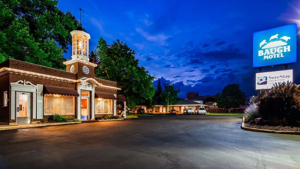 A motel with a central tower, a sign for Baugh Motel, and a SureStay Collection sign. - Baugh Motel, SureStay Collection by Best Western (Logan)