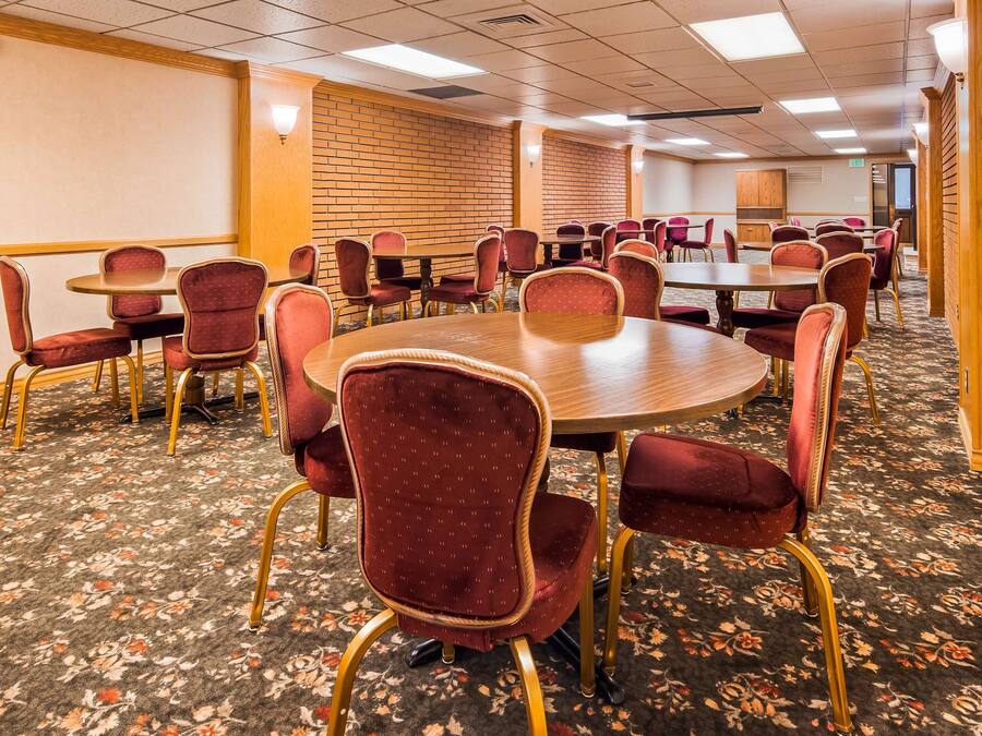 A conference room with round tables and red upholstered chairs, carpeted floor, and wooden paneling on the walls.