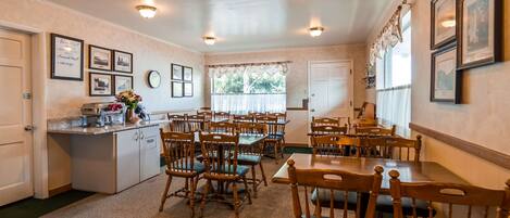 A dining area with wooden tables and chairs, a buffet counter, and framed pictures on the walls.