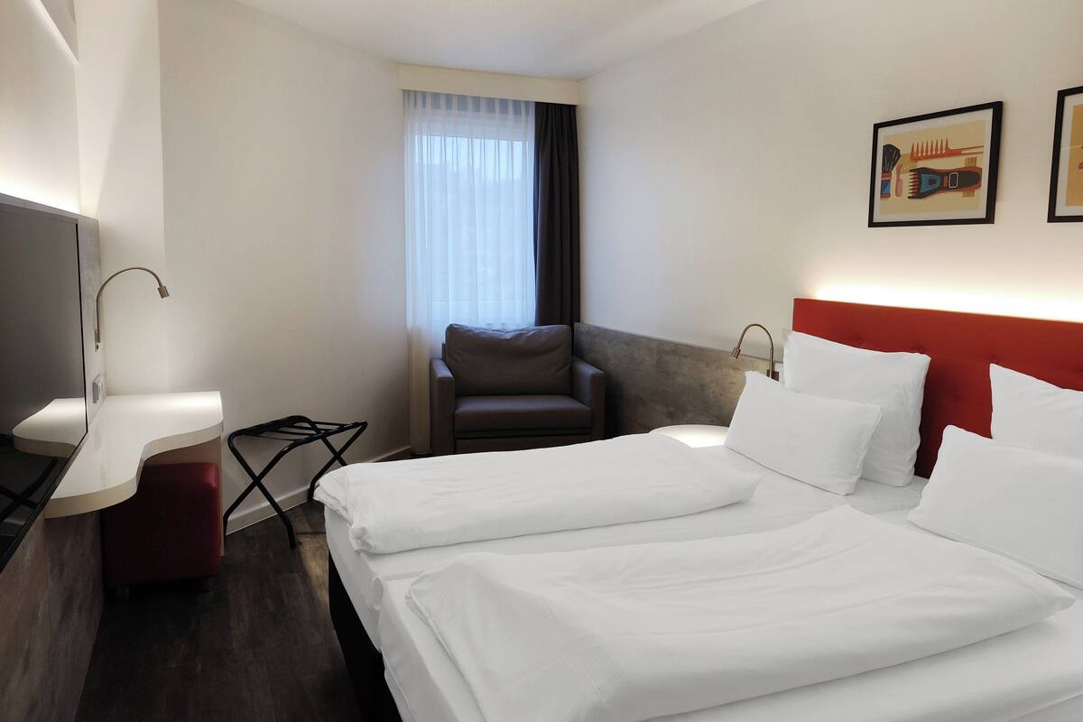 A hotel room with two beds, a desk, a chair, and a TV.