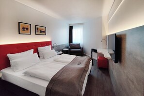 A hotel room with a large bed, a desk, a chair, a TV, and artwork on the wall. - Garner Hotel Wiesbaden City by IHG (Wiesbaden)