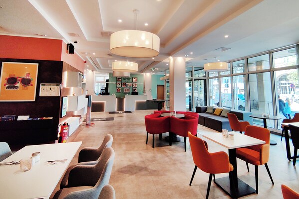 A modern restaurant with a central seating area, a bar, and a large window offering a view of the street. - Garner Hotel Wiesbaden City by IHG (Wiesbaden)