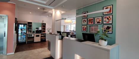 Zona de recepción con mostrador, refrigerador y pared decorada con cuadros enmarcados.
