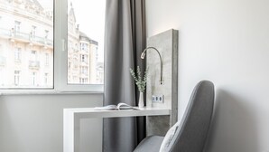 A modern room with a window, a grey chair, a white desk, and a grey curtain. - Garner Hotel Wiesbaden City by IHG (Wiesbaden)