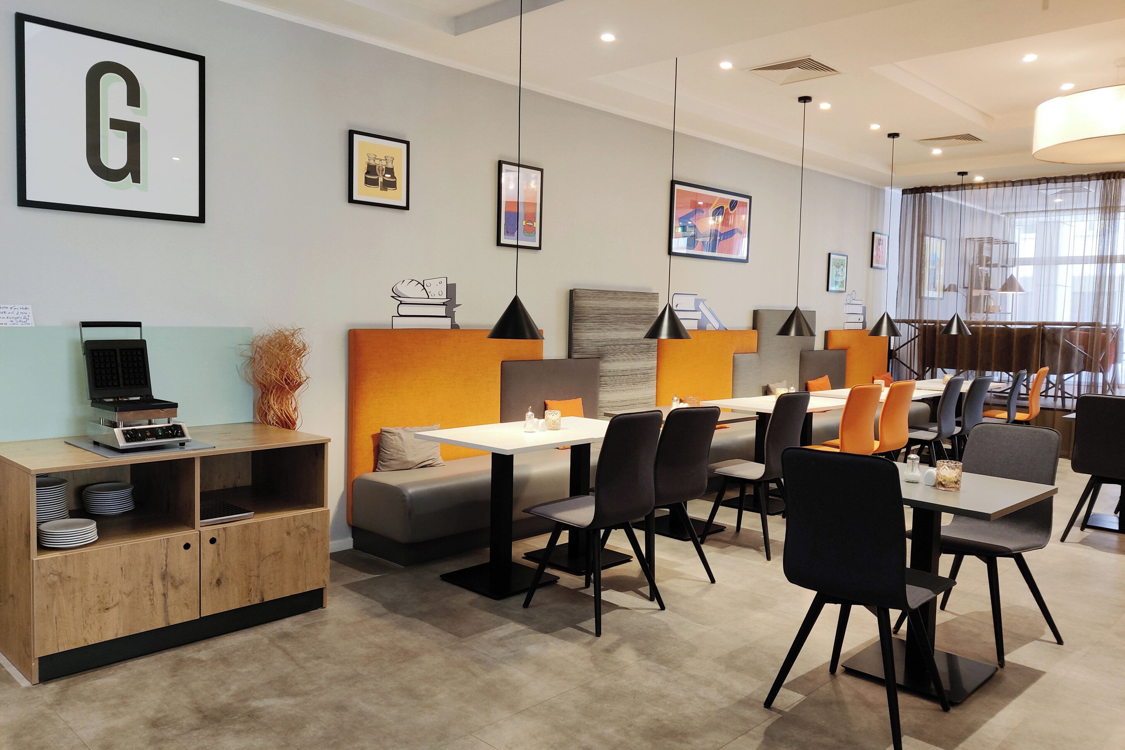 A modern dining area with tables and chairs, a wooden cabinet with a computer, and framed artwork on the walls.