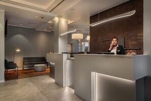 A modern reception area with a receptionist, a sofa, and a desk. - Garner Hotel Wiesbaden City by IHG (Wiesbaden)